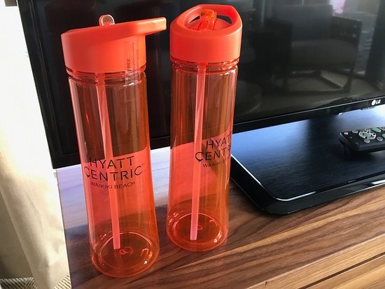 two orange water bottles branded with a hotel logo on a hotel room side table. Eco Tips for Hotels ditch plastic single use water bottles for branded refillable Water Bottles