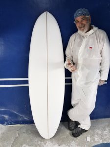 surfboard shaper in protective overalls standing next to a white surfboard he has made
