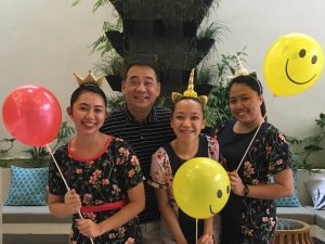 Three Front Office staff wearing unicorn head bands and holding smiley face balloons, with Dante Cruz General Manager of Ferra Hotels