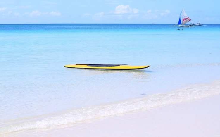 Yellow paddle board in the water of White Beach Boracay Island with a local paraw boat in the background. Article Boracay Ranked 10th Among Worlds Best islands, by MY RANGGO Philippine Hospitality Magazine