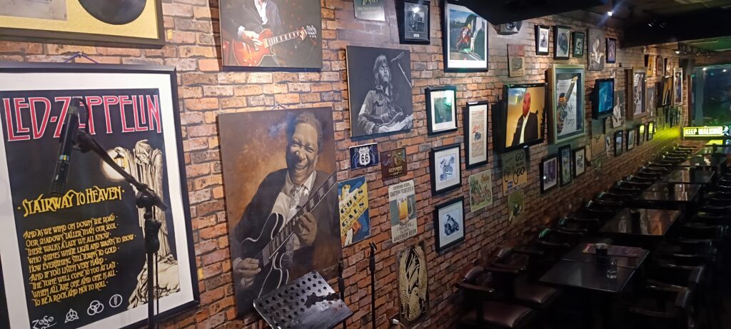 A long brick-designed wall with a gallery of band and singer photos and images, with wooden tables and chairs at The Roadhouse Manila Bay